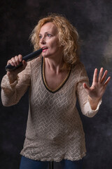 A blonde woman simulates singing at a concert using a remote control as a microphone