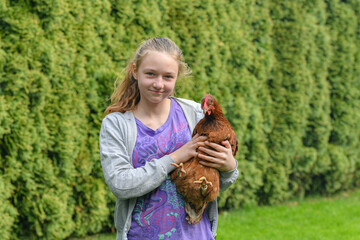 The girl caught the chicken and holds it in her hands.