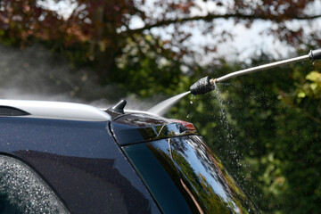 A driver washes a black car with a high-pressure water jet at his home.
