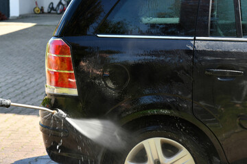Washing a black car with a high pressure water jet at home.