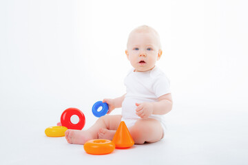 a baby boy in a white bodysuit is sitting playing with a multicolored pyramid smiling on a white background