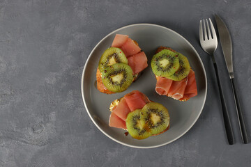 Sandwiches with soft cheese, jamon and kiwi on gray plate. Delicious and healthy breakfast