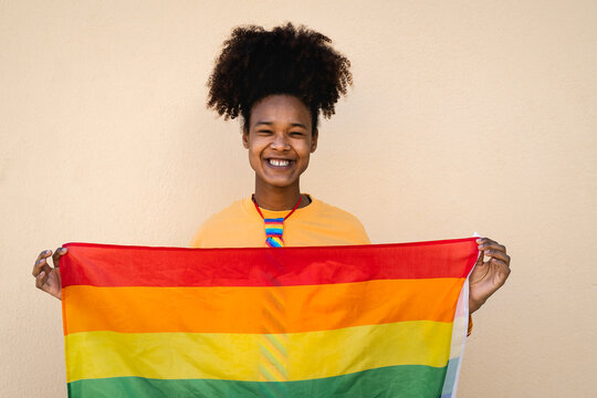 Happy African gay woman celebrating pride holding rainbow flag outdoor - LGBT concept