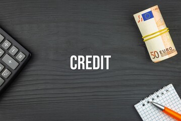 CREDIT - word (text) and euro money on a wooden background, calculator, pen and notepad. Business concept (copy space).