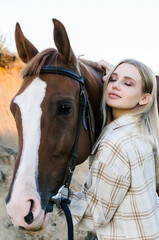 Fototapeta premium Young woman hugs her horse close-up on ranch. Pleasure, love and care for animals, nature country lifestyle. warm natural brown tones in sunset