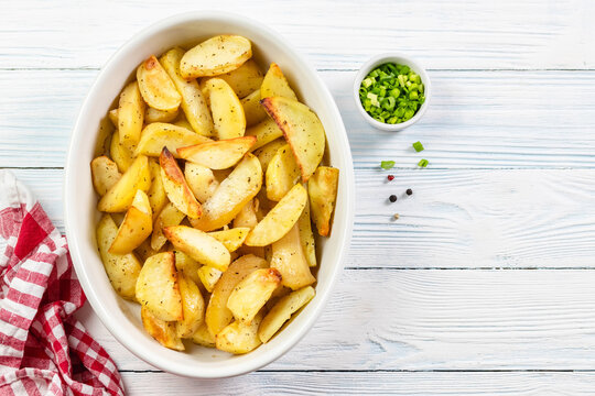 Seasoned baked potato wedges in baking dish on wooden background. Top view, copy space.