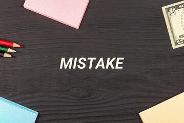 MISTAKE - text, money dollars, stickers and colored pencils on a black wooden table. Business concept: buying, selling, commerce (copy space).