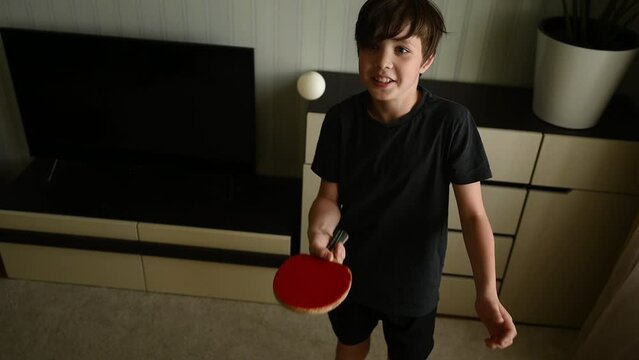 A teenager at home conducts table tennis training. The child is practicing hitting the ball with a racket. Training at home. A teenager does sports