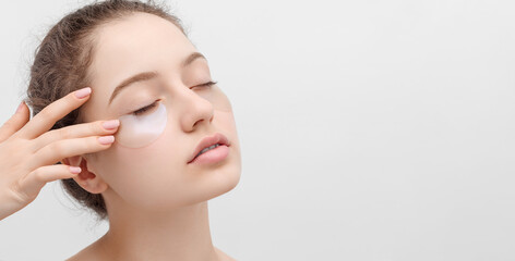 Close up shot of a young woman applying eye pads. Eyes closed, gently touches her face. Banner.