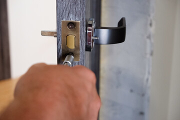 Installing door handle with lock, locksmith fixes bolt on latch plate.