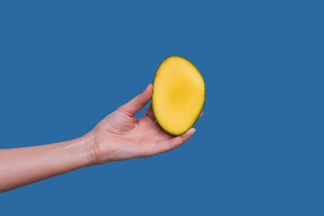 Young woman hold fresh sliced mango fruit in hand besides blue background.