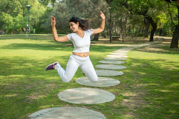 Young indian fitness woman wearing white sportswear jumping carefree at park .  Mental health, fun...