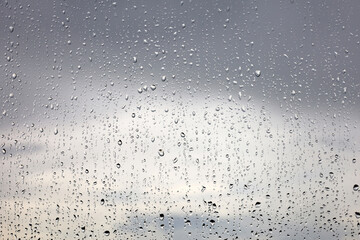 Raindrops on the window glass on blurred background of storm sky with clouds. Water drops, weather during rain