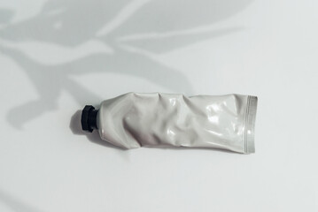 Mockup of crumpled tube of cream with leaves shadows.