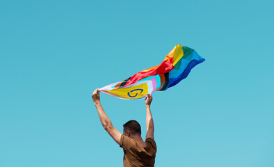 waving a progress pride flag above his head - obrazy, fototapety, plakaty