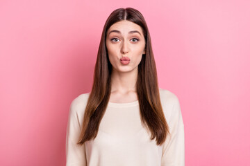 Fototapeta premium Portrait of attractive flirty brown haired girl sending air kiss isolated over pink pastel color background