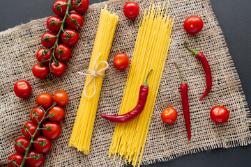 Top view of fresh vegetables and raw pasta on sackcloth on black background.