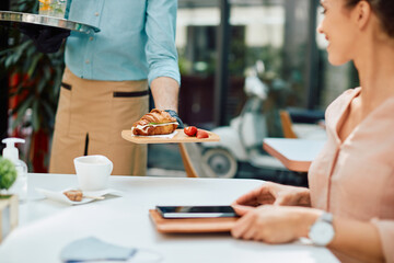 Close up of waiter serving croissant sandwich to woman in cafe.