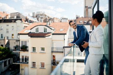 Happy businessman and his black coworker enjoy in balcony of their office building.