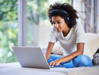 Whiling away the day online. Shot of a young woman sitting at home using a laptop and wearing...