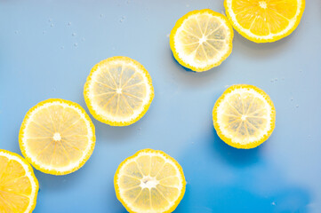 Lemon slices in water on blue background. Swimming lemon slices background.