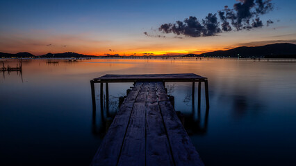 Fototapeta na wymiar Warm Horizons. Pier Over Lake Against Sky During Sunset.