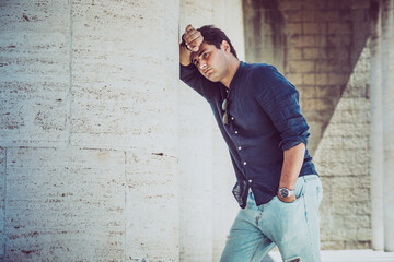 Obraz premium Young depressed and tired man outdoors leaning with one arm on a white wall. Casual dress.
