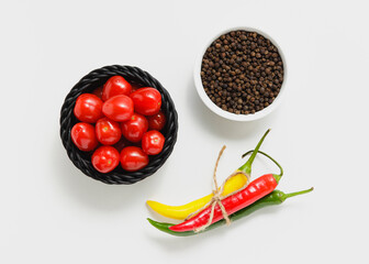 Cherry tomatoes in black basket with pepper on white background.
