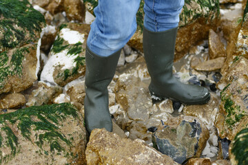 Rubber boots on stones with seaweed in the ocean