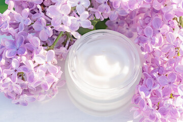 Top view of jar with face cream and lilac flowers on a light wooden background, place for text. Natural organic cosmetics concept.