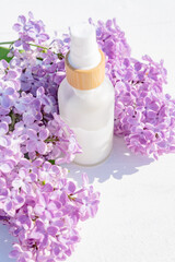 Close-up of a white bottle with natural cosmetic cream and a branch of lilac on a white background. Cosmetic beauty concept.