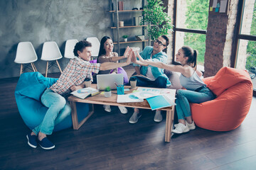 Full body photo of group friendly satisfied people sit beanbag give high five clapping each other...