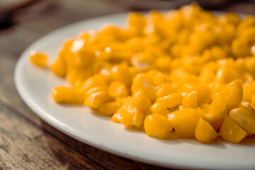 Macro of sweet corn over the white plate on wooden table. The photo is perfect for food background, brochure and pamphlet advertising.
