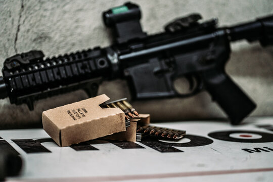 Assault rifle with red dot sight next to a box with ammunition