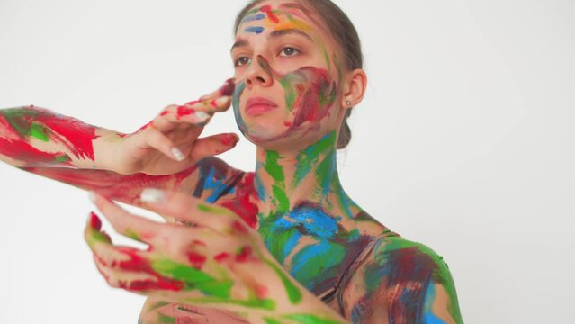 Brunette woman with her hair in a bun, dancing with her hands and body, portrait. Woman soiled face and body in paint handprints stripes, dancing smoothly on white background. Concept of creativity