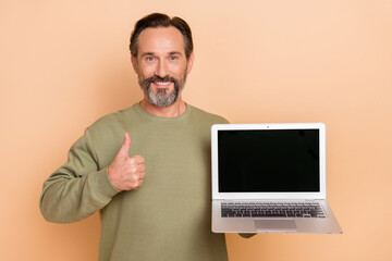Portrait of attractive trendy cheerful man holding laptop showing thumbup ad isolated over beige...