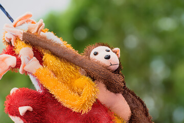 A naughty soft toy monkey dangling with other toys attracts the attention of kids . The background of soft diffused green trees makes the toys stand out prominently.