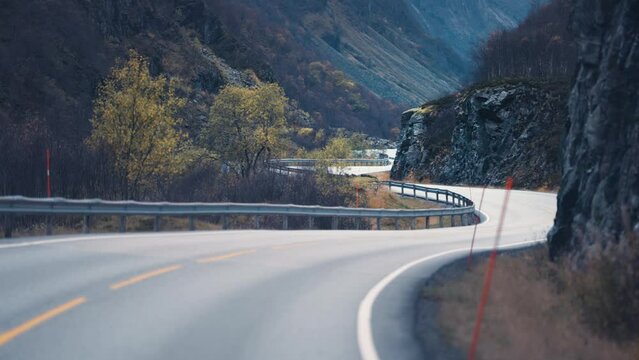 Two-lane country road snakes between the steep rocky slopes. Slow-motion, pan forward.