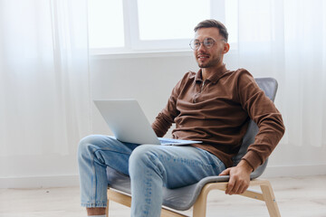 Fototapeta premium Modern Profession offer. Happy cheerful guy man in eyewear touch chair smile project think about right decision for work screen sitting in chair at home. Remote Job Distant Work Communication concept