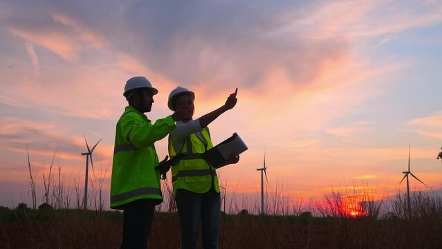 Engineer wearing uniform ,helmet inspection and survey work in wind turbine farms rotation to generate electricity energy. Green ecological power energy generation wind sustainable energy concept.