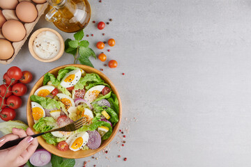 Girls' hands holding healthy vegetarian breakfast bowls flat-lay. Healthy salad of fresh vegetables - tomatoes, egg, Onion. high angle view of a nutritious vegetable salad with boiled egg slices.