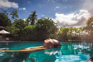 Woman relaxing and floating in swimming pool. Reflection in the water.