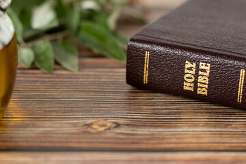 Holy Bible Book with golden text, green olive branch, and oil in a jar on a wooden table. Christian...