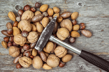 Hammer and pile of assorted nuts on a wooden background