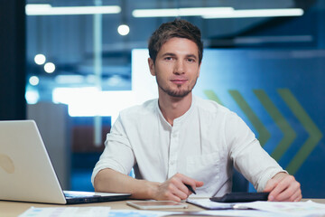 Portrait of a young businessman man in modern clothes working with documents and looking seriously at the camera