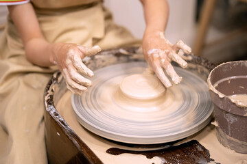 Fototapeta na wymiar Human hands and potter's wheel. Hands of a child making a cup on a potter's wheel.