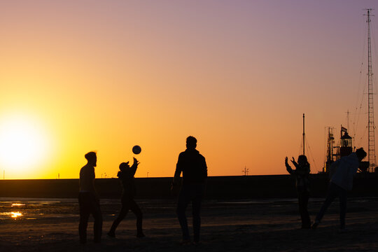 silhouette of friends playing volleyball on beach with sunset
