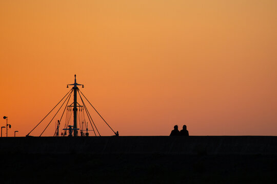 silhouette of a couple at beach at sunset with sailboat in background