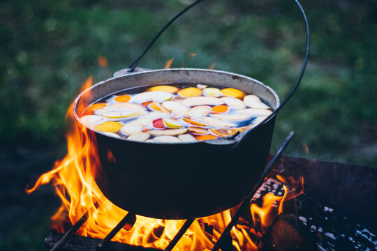 Fruit compote is cooked in a cauldron on the fire, outdoors. 