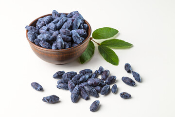 Honeyberry (Lonicera caerulea). Sweet honeysuckle berries in a clay bowl on a white background